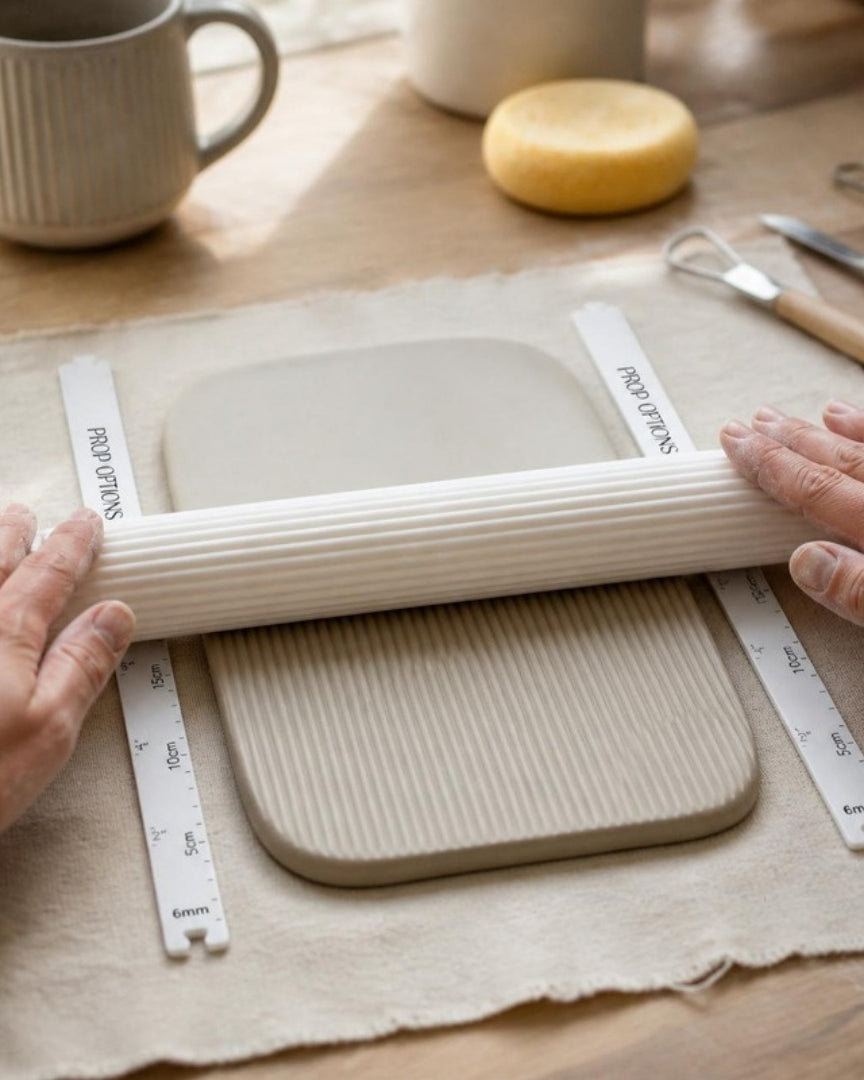 Clay thickness guides either side of a stoneware slab with a Prop Options reeded texture roller
