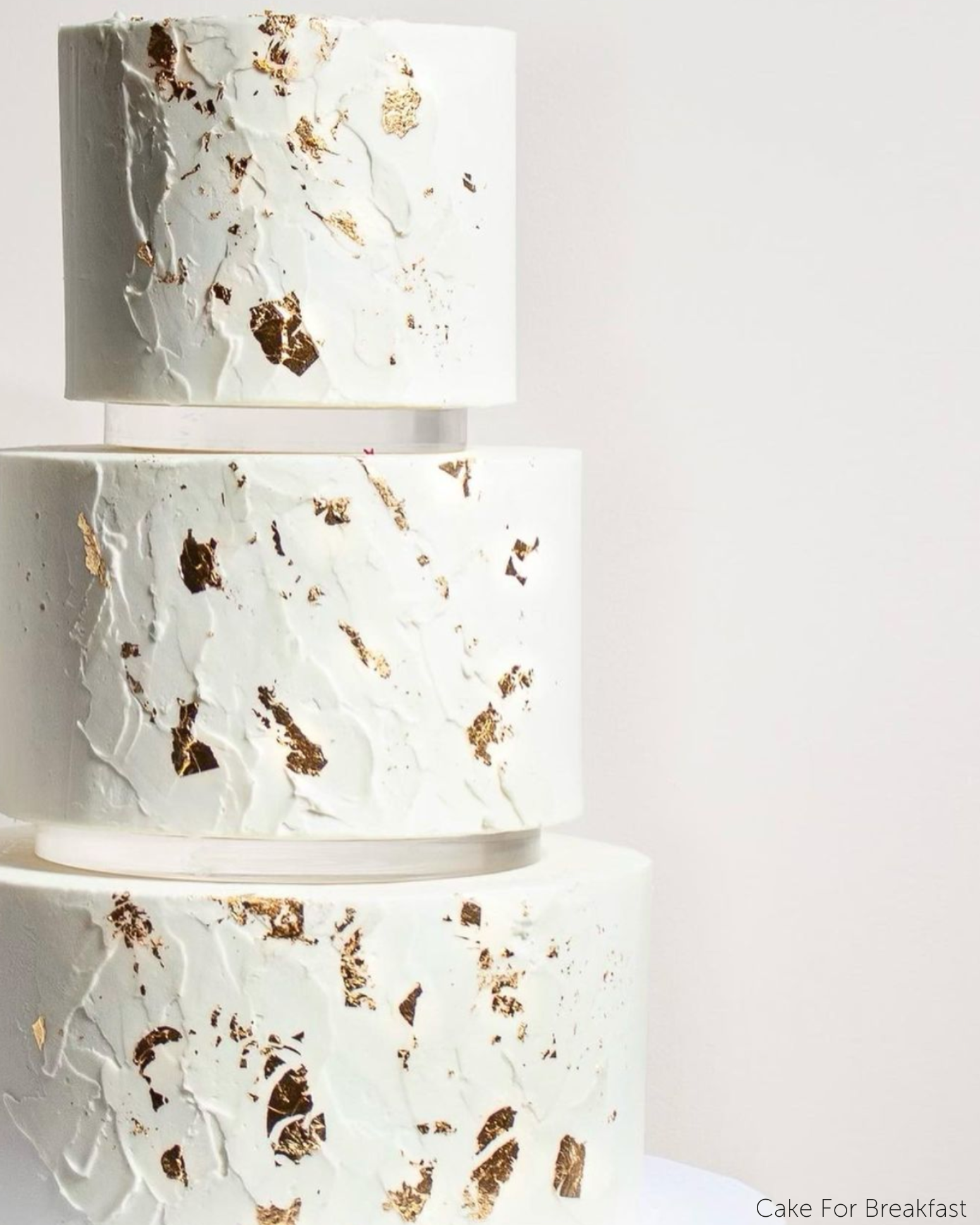 A plain white three tier cake with subtle gold decorations, each layer is separated by a 15mm Acrylic Cake Separator - Prop Options