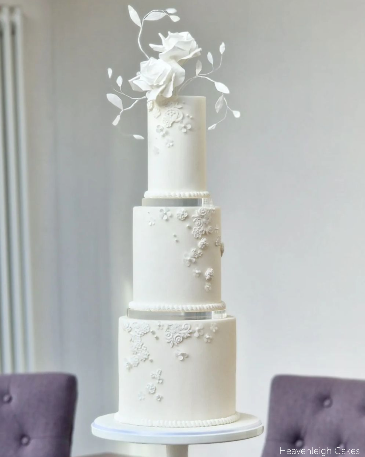 A plain white three tier cake with subtle white floral icing on each layer and bright white flowers on the top, each layer is separated using a 15mm Acrylic Cake Separator - Prop Options