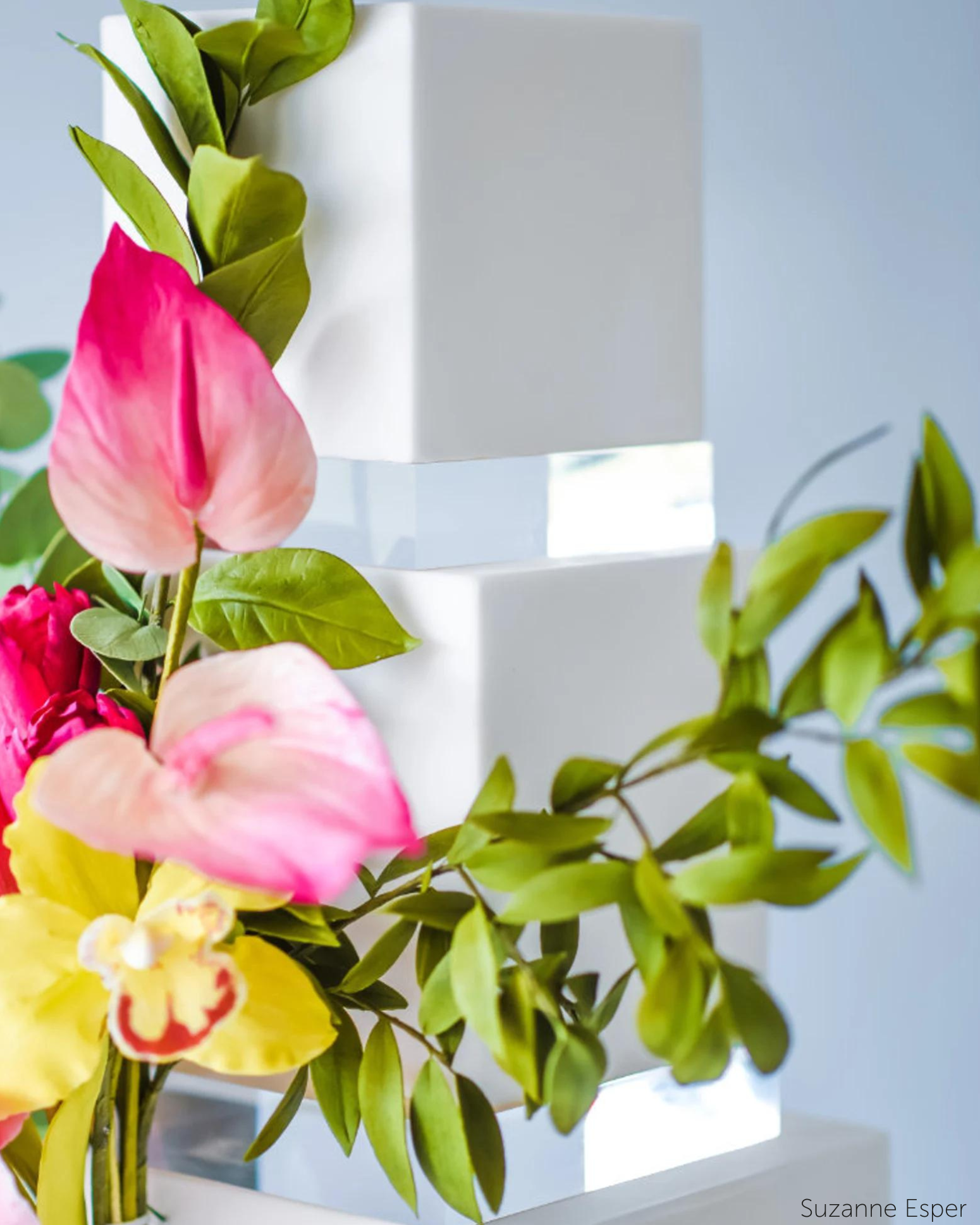 A plain white cake with bright yellow and pink flower decorations, there are 30mm Square Acrylic Cake Separators between each layer - Prop Options