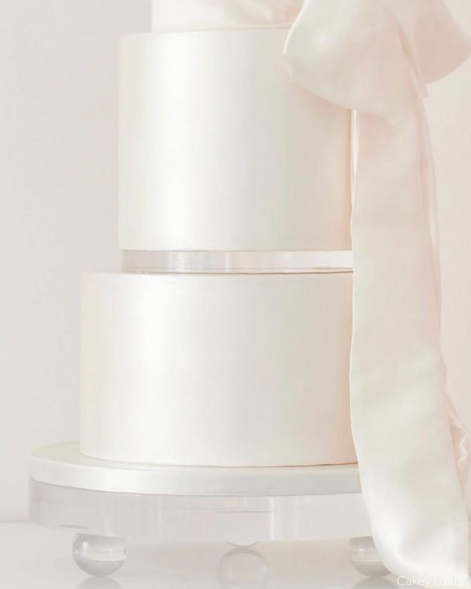 Close up of a plain white multilayer cake with a white ribbon, two of the layers are separated with a 15mm Acrylic Cake Separator - Prop Options