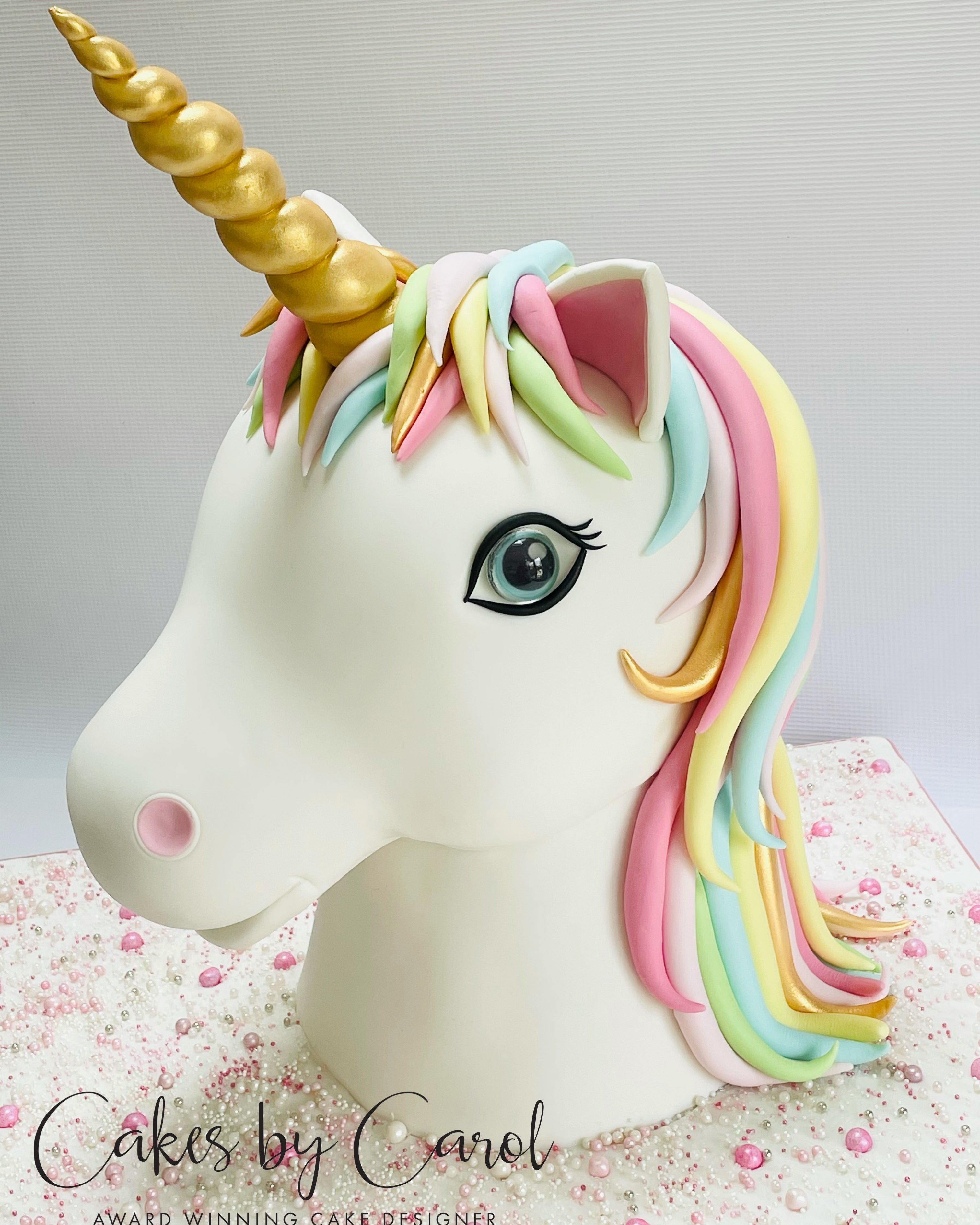 Unicorn cake with colorful mane and gold horn on a light background