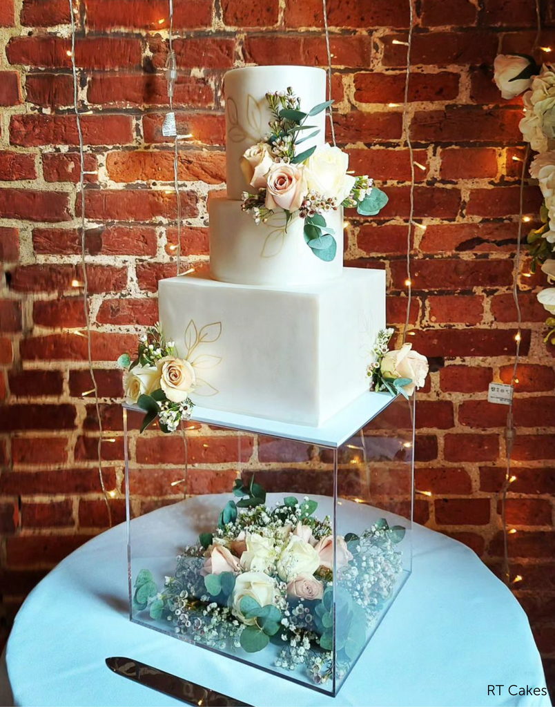 Square Acrylic Fillable Plinth filled with roses and leaves holding up a multitiered cake with rose decorations - Prop Options