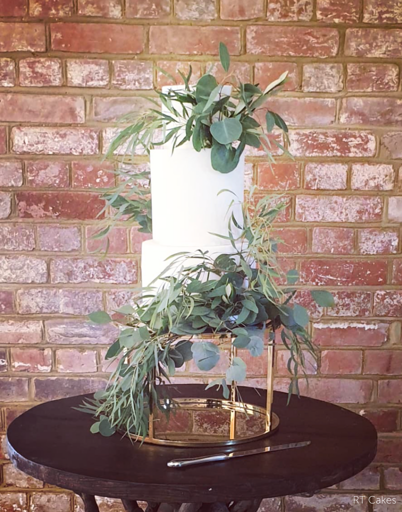 Gold Round Metallic Plinth holding up a plain white cake covered in green leaves - Prop Options