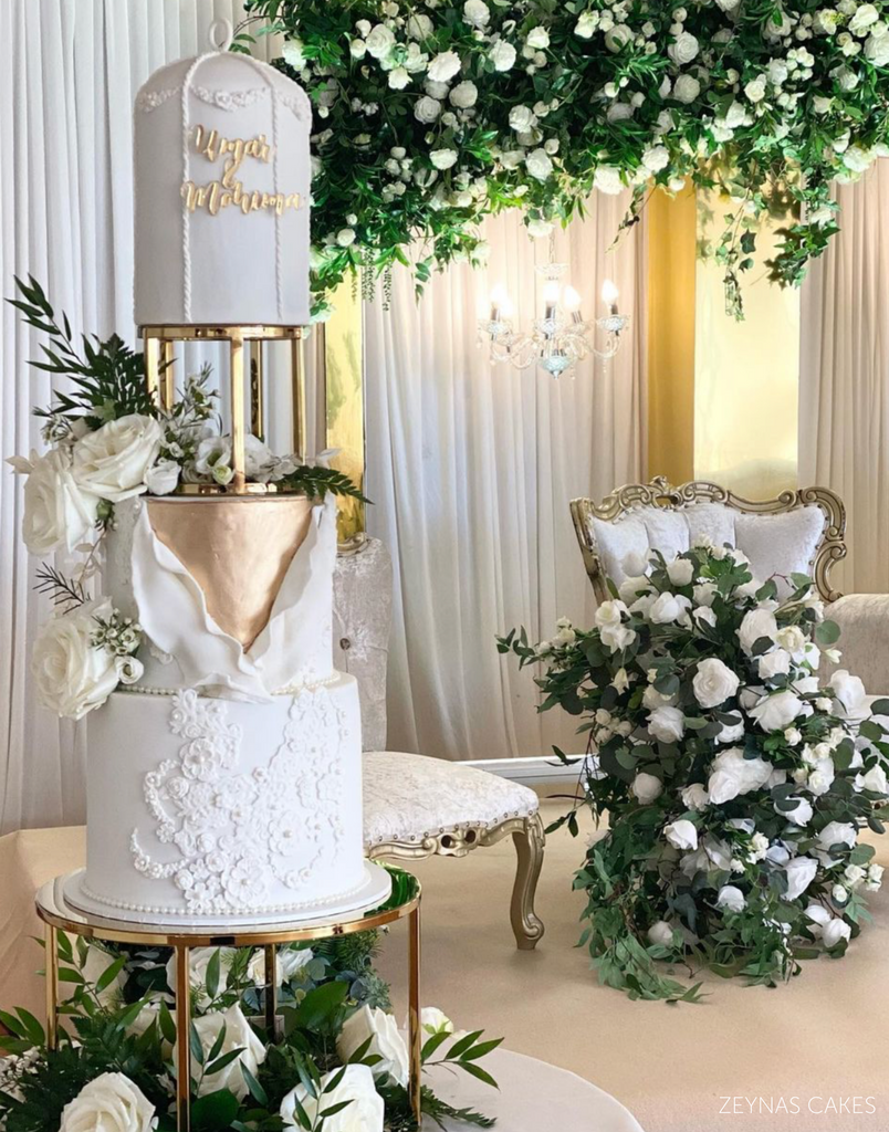 Gold Round Metallic Plinth holding up a tall white cake decorated with white roses and gold lettering - Prop Options
