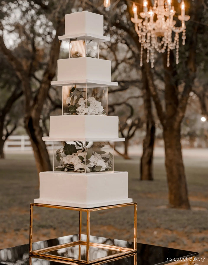 Gold Square Metallic Plinth holding up a multilayered wedding cake, the layers are spaced out with square acrylic tiers that are filled with white flowers - Prop Options