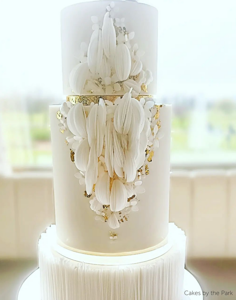 A close up of a white three tier cake with white and gold petal decorations on the front, each tier is separated by a 15mm Acrylic Cake Separator - Prop Options