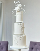 A plain white three tier cake with subtle white floral icing on each layer and bright white flowers on the top, each layer is separated using a 15mm Acrylic Cake Separator - Prop Options