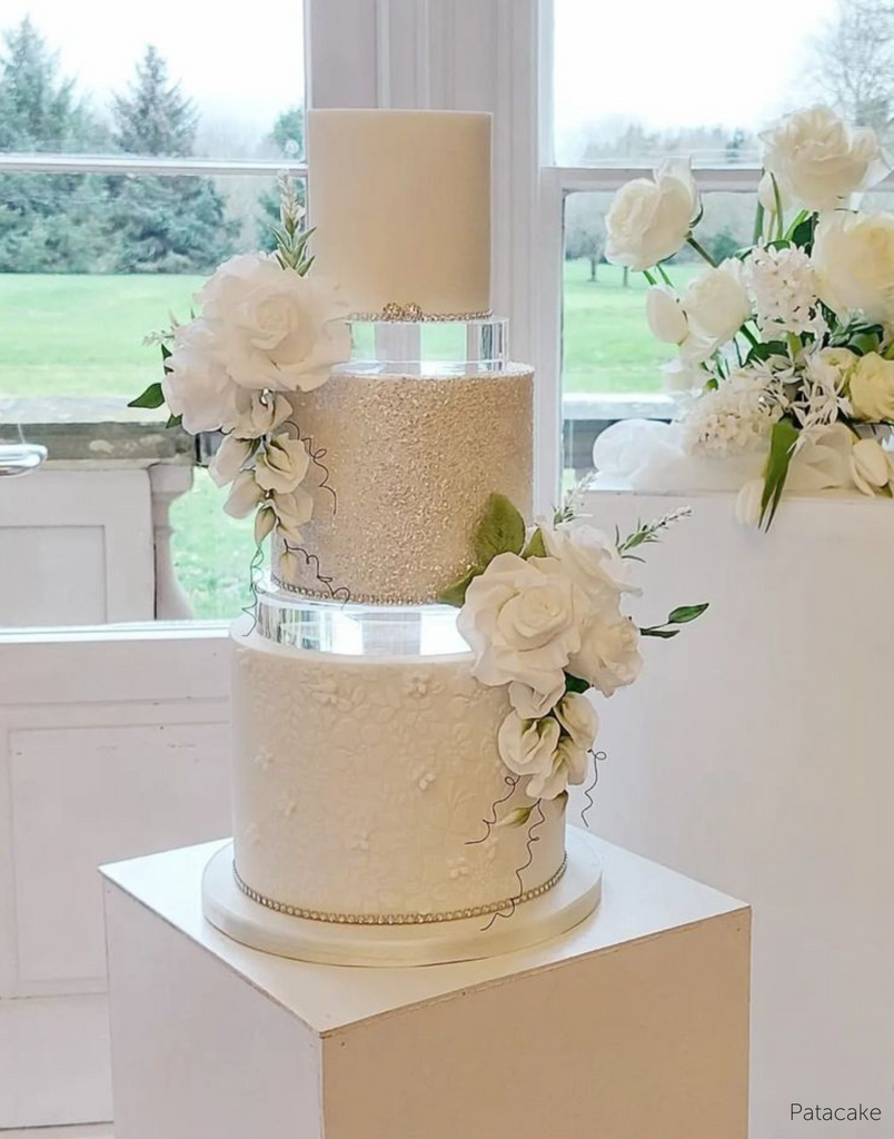 A three tiered white cake with a glittery middle layer and white flower decoartions, each layer is separated using a 30mm Round Acrylic Cake Separator - Prop Options