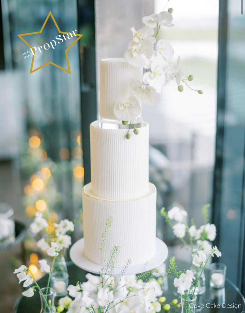 PropStar winning submission - a white circular cake with white flower decorations, the top two layers are separated by a 30mm Round Acrylic Cake Separator - Prop Options