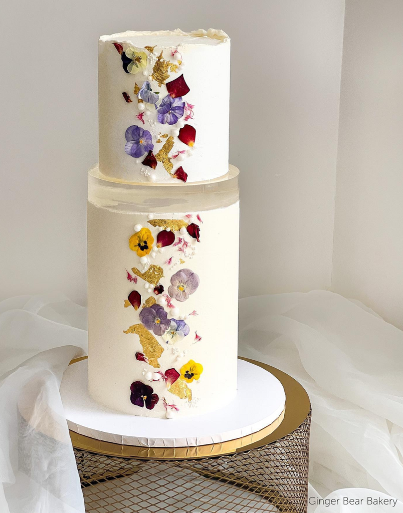 A two tier plain white cake with a strip of floral decorations down the middle, the two tiers are separated by a 30mm Round Acrylic Cake Separator - Prop Options