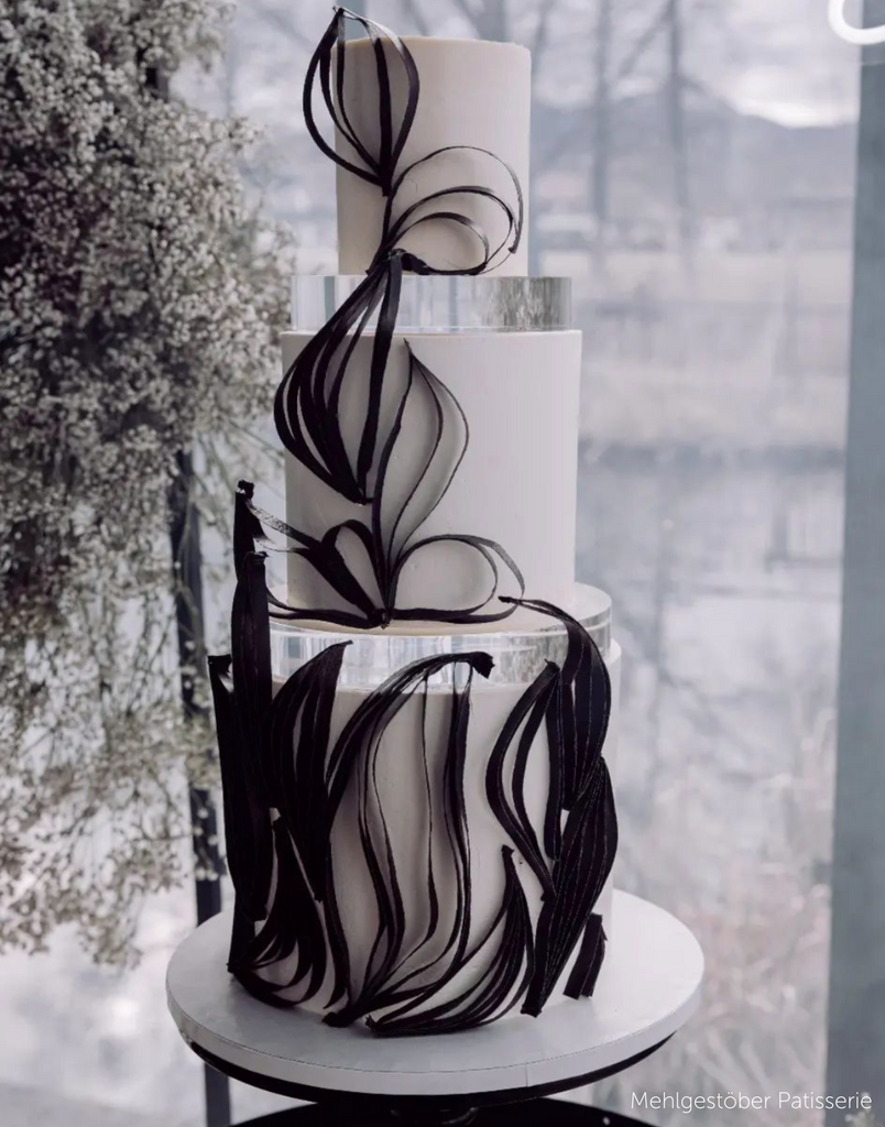 A white three tier cake with elegant black decorations, the layers are separated with 30mm Round Acrylic Cake Separators - Prop Options