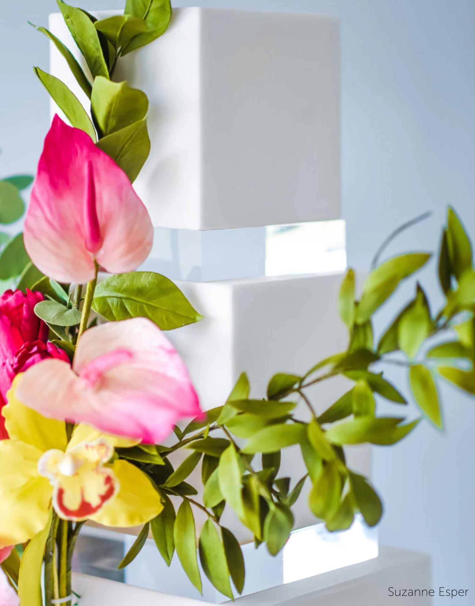 A plain white cake with bright yellow and pink flower decorations, there are 30mm Square Acrylic Cake Separators between each layer - Prop Options