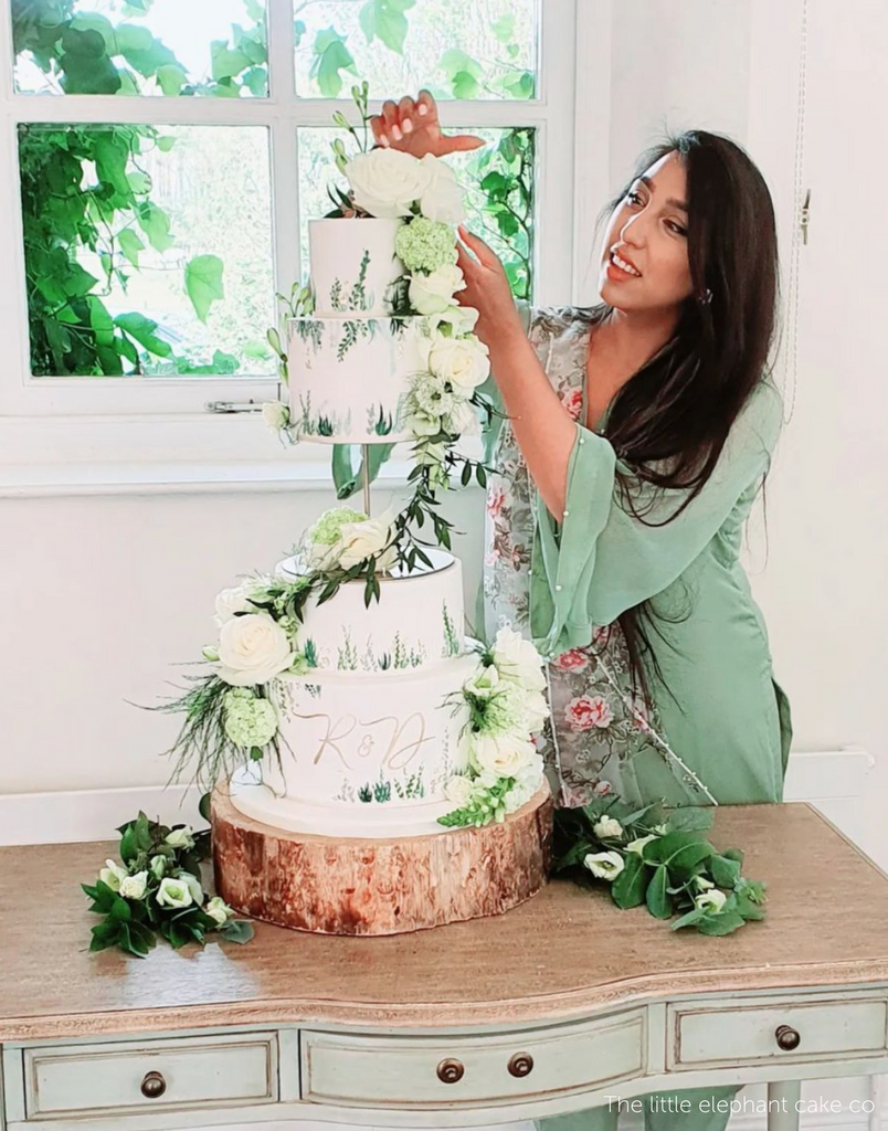 A four layer white cake with white and green floral decorations, the middle two tiers are separated using a PropSecure® Adjustable Central Bar Cake Separator - Prop Options