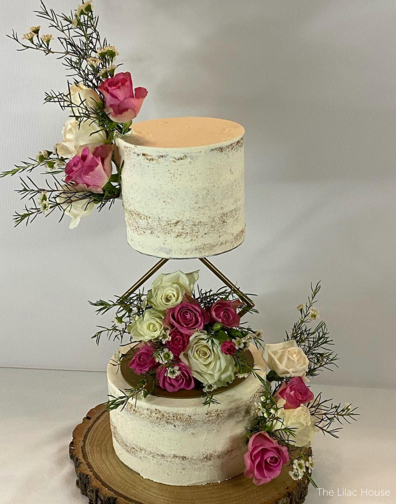 A rustic white two tier cake with white and pink roses, the tiers are separated with a Diamond Cake Spacer - Prop Options