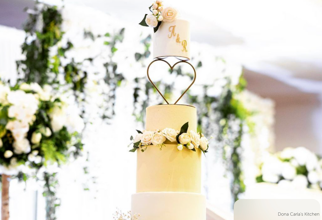 A four tier yellow and cream cake with white roses and the initials A & R in gold on the top tier, a Heart Tier Separator is between the top two layers - Prop Options