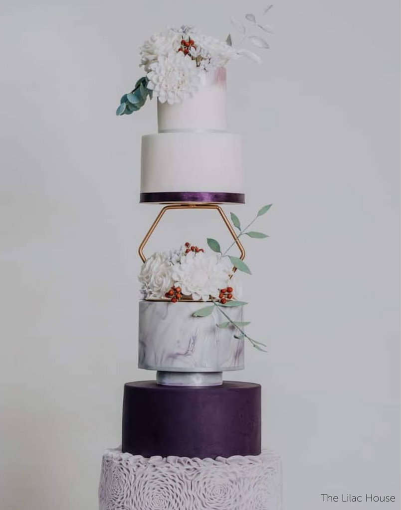 An elegant multitiered white and purple cake with delicate floral decorations, the middle of the cake is separated using a Hexagon Tier Separator - Prop Options