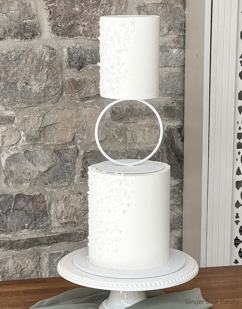 A simple white two layer cake with subtle pearl decorations along the side separated by a Hoop Tier Separator - Prop Options