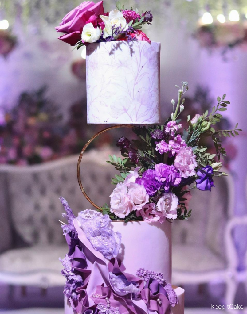 A purple three layer cake covered with purple flowers, the top two tiers are separated by a Hoop Tier Separator - Prop Options