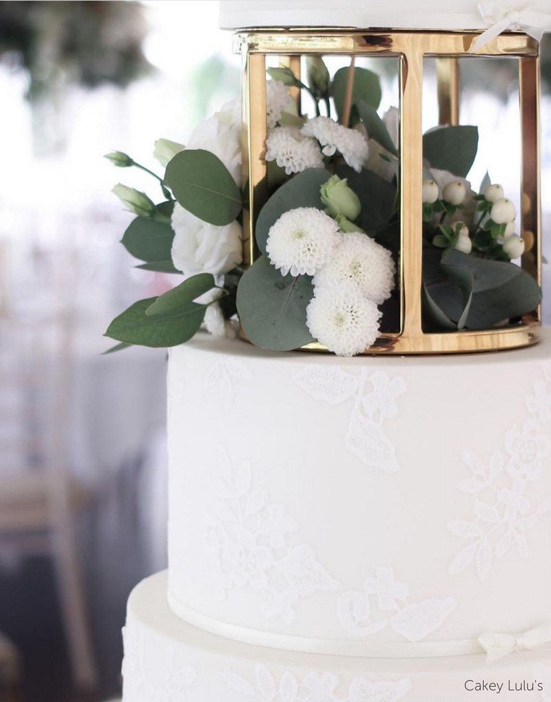 A close up of a plain white cake separated by a 6" Round Metallic Cake Spacer with white flowers inside - Prop Options
