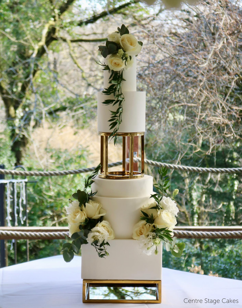 A multilayered white cake with white roses separated using a Rectangle Metallic Cake Spacer - Prop Options
