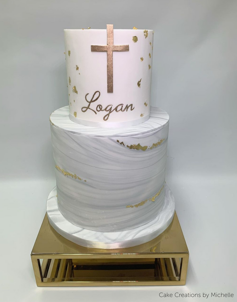 A circular white cake with the name Logan written in gold lettering sat on top of a Rectangle Metallic Cake Spacer - Prop Options