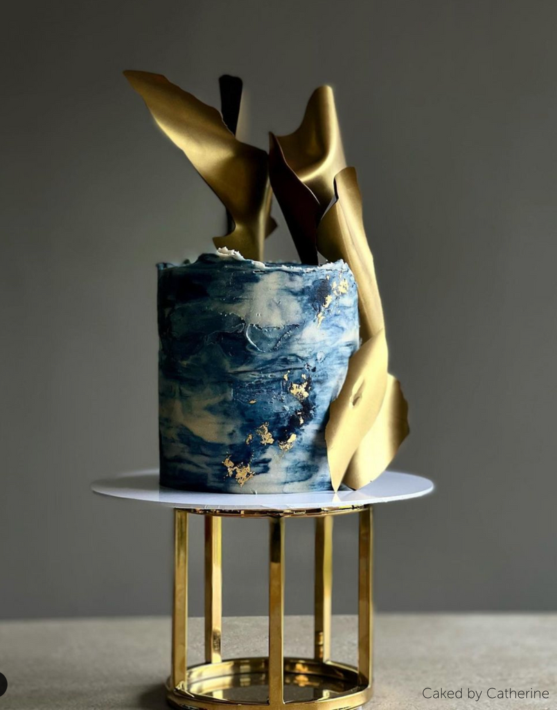 A dark blue marbled cake with gold decorations stood on a 6" Round Metallic Cake Spacer - Prop Options