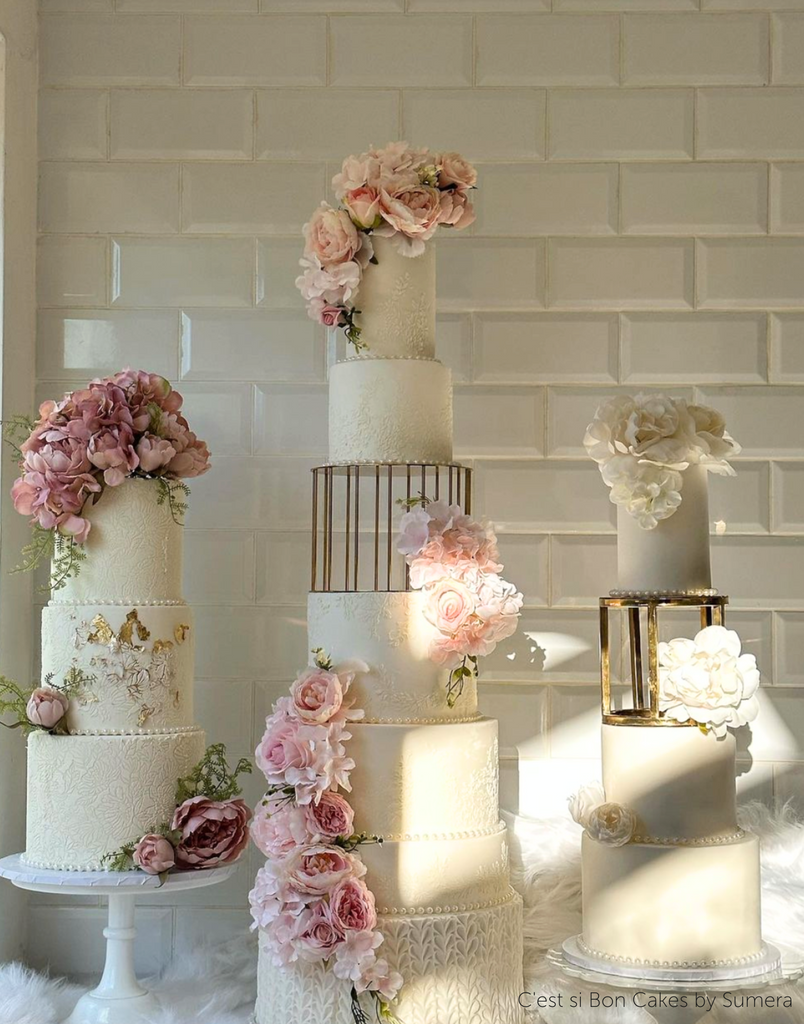 Three tall white wedding cakes covered in pink flowers, the one on the right separated the top tiers using a 6" Round Metallic Cake Spacer - Prop Options