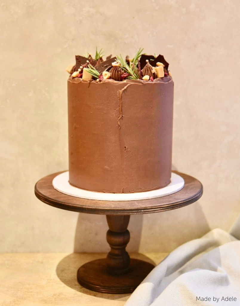 A brown cake with chocolate on the top stood on The Original Scandinavian Birch Cake Stand - Prop Options