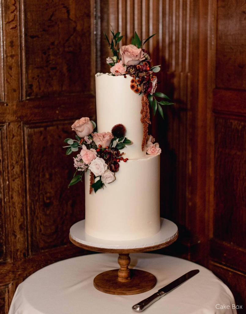 A plain white cake with pink and red flowers stood on The Original Scandinavian Birch Cake Stand - Prop Options