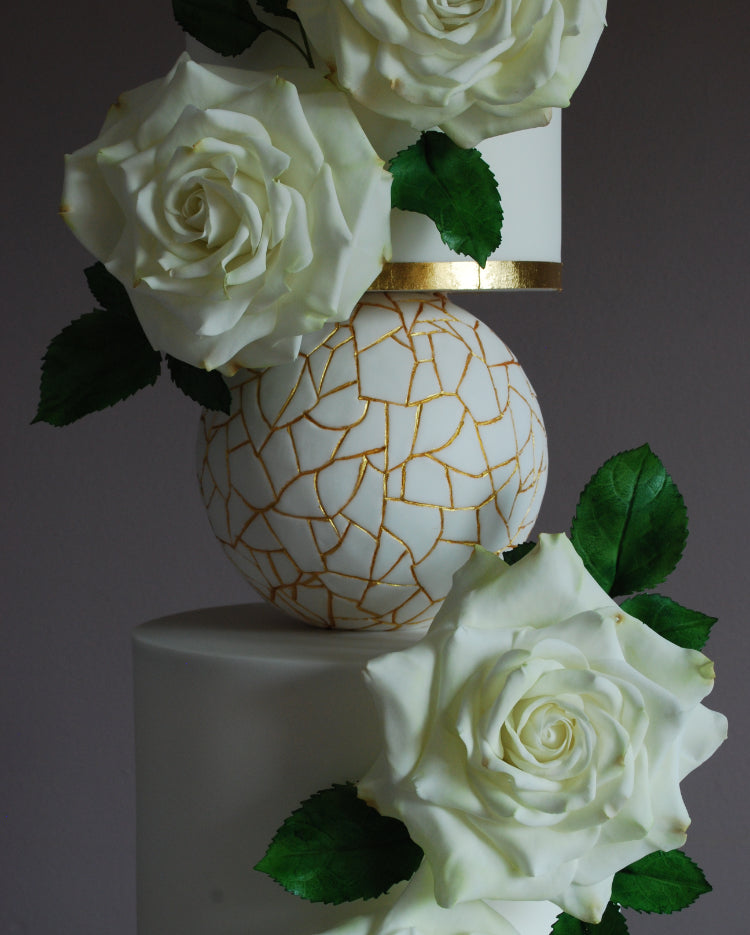 Prop Options Adjustable cake separator with central bar in use expertly decorated with a white and gold design with white roses