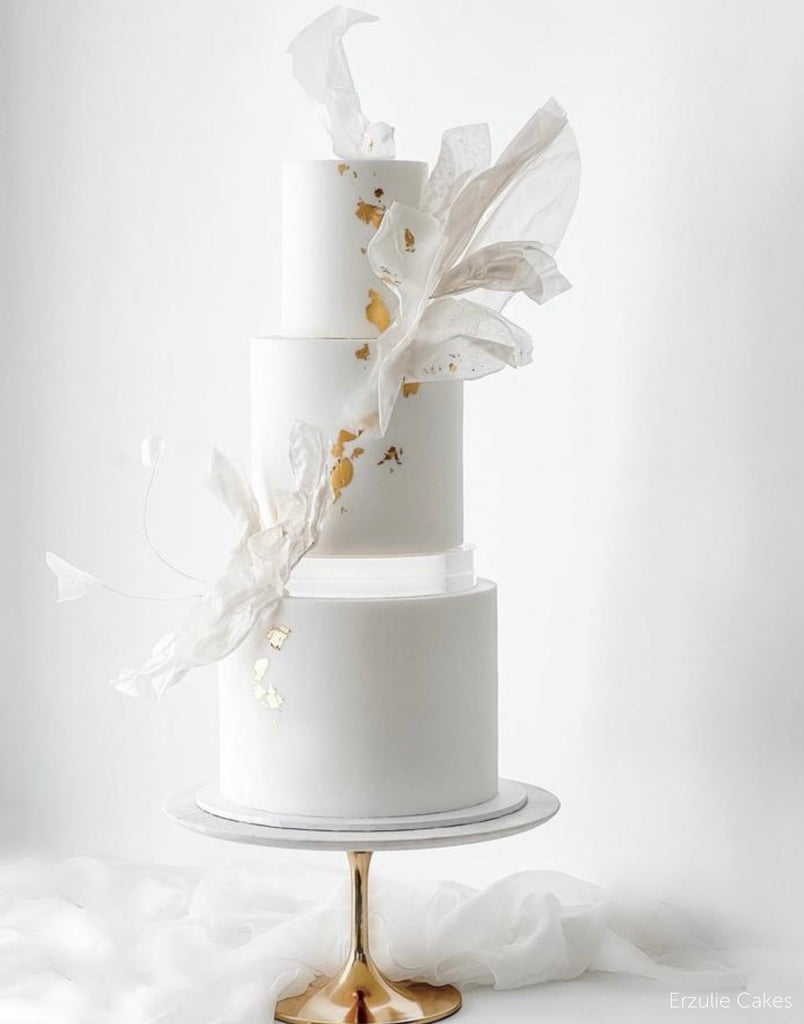 A plain white cake with subtle gold decorations and white fabric, the bottom and middle layer are sepaarted by a 30mm Round Acrylic Cake Separator - Prop Options