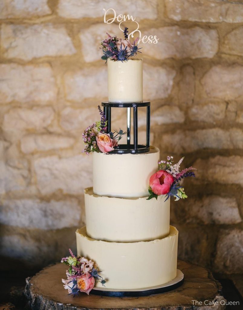 A white four layer cake with pink flowers, the top two tiers are separated by a 6" Round Metallic Cake Spacer - Prop Options