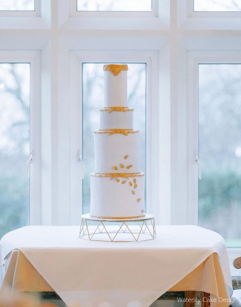 Geometric Cake Stand holding a plain white four layer cake with subtle yellow decorations along the edges and bottom two layers - Prop Options