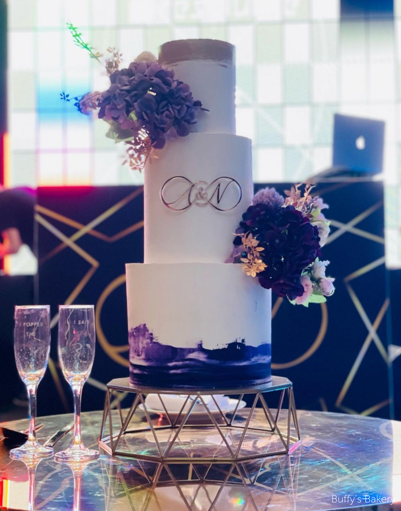 Geometric Cake Stand holding a three layer white and purple cake decorated with purple flowers and the initials A & N on the front - Prop Options
