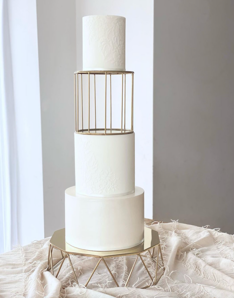 Geometric Cake Stand holding a plain white three layer cake with a gold birdcage separator between the top two layers - Prop Options