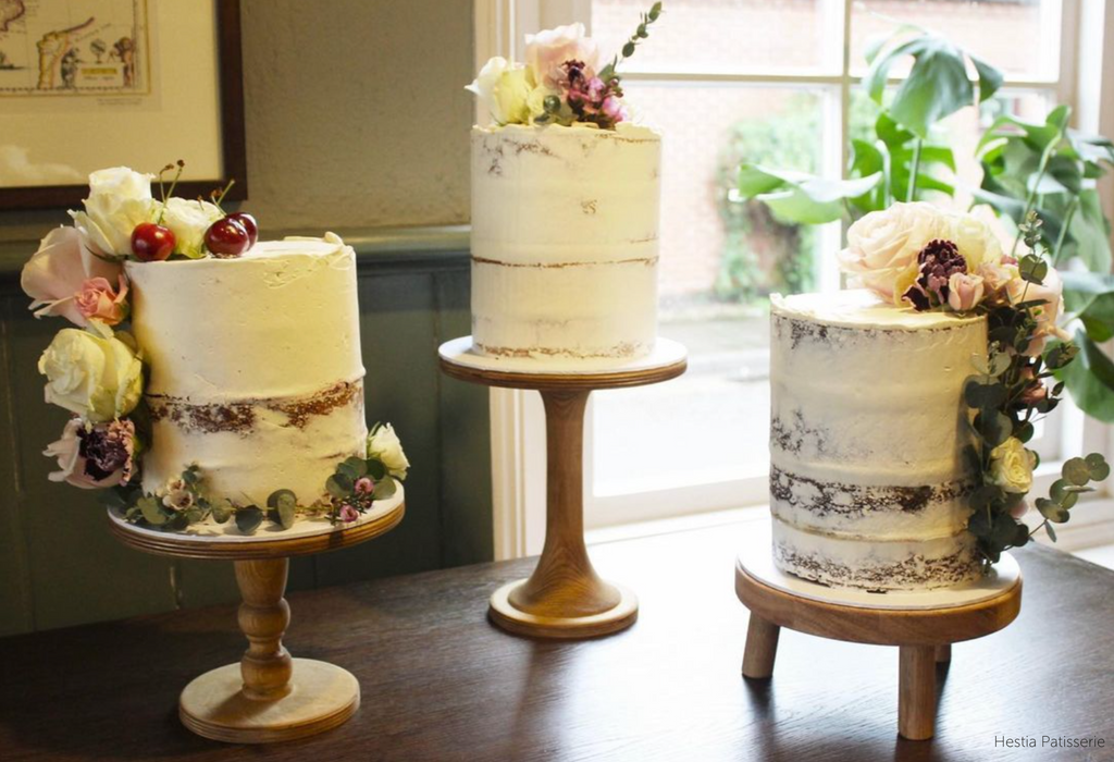 Three white floral cakes stood on a trio of Hourglass Scandinavian Birch Cake Stands - Prop Options