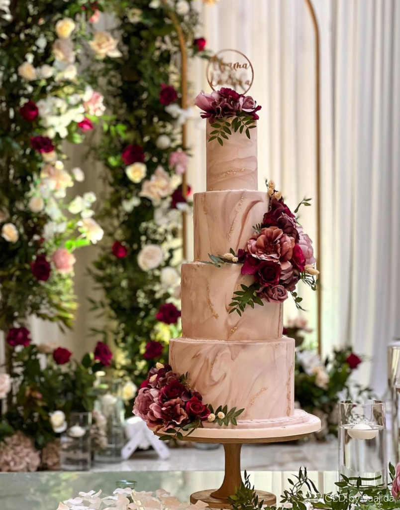 A marbled pink cake covered in pink flowers stood on The Hourglass Scandinavian Birch Cake Stand - Prop Options