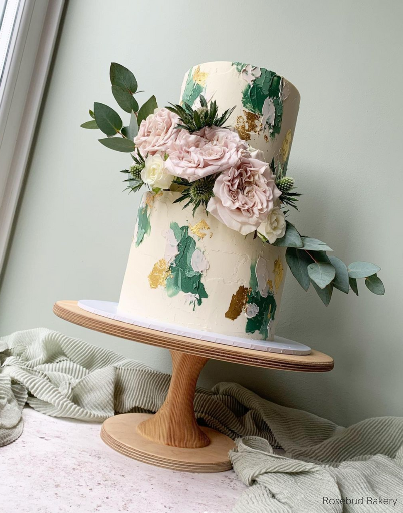 A white cake with green and pink florals stood on The Hourglass Scandinavian Birch Cake Stand - Prop Options