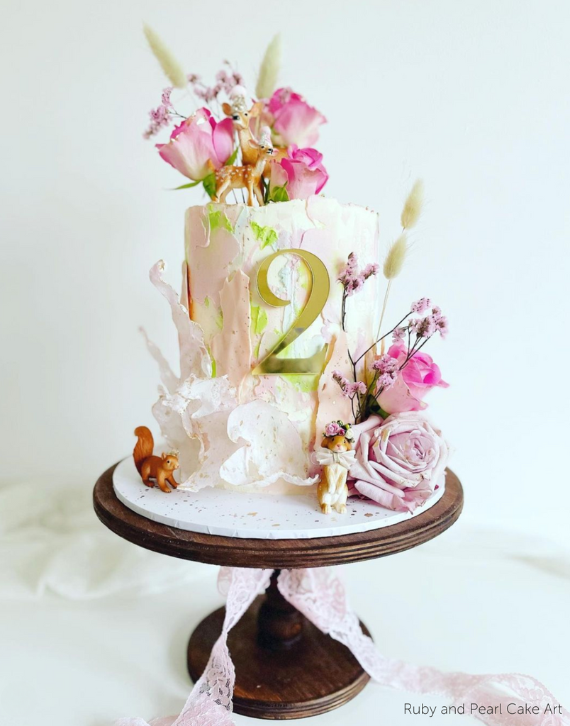 A light floral birthday cake with the number 2 in gold lettering on the front stood on The Original Scandinavian Birch Cake Stand - Prop Options