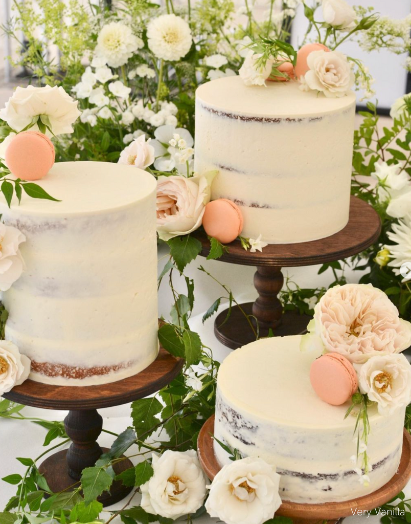 Three rustic white cakes covered in white flowers and peach coloured macarons stoof on a trio of Original Scandinavian Birch Cake Stands - Prop Options