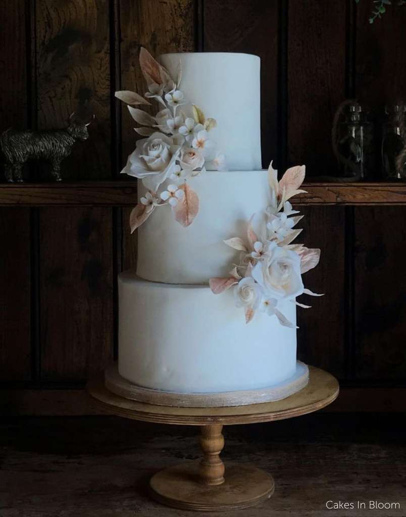 A plain white cake covered in light coloured flowers stood on The Original Scandinavian Birch Cake Stand - Prop Options