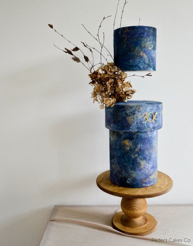 A marbled dark blue cake with brown florals and the number 30 in gold lettering stood on The Teardrop Scandinavian Birch Cake Stand - Prop Options