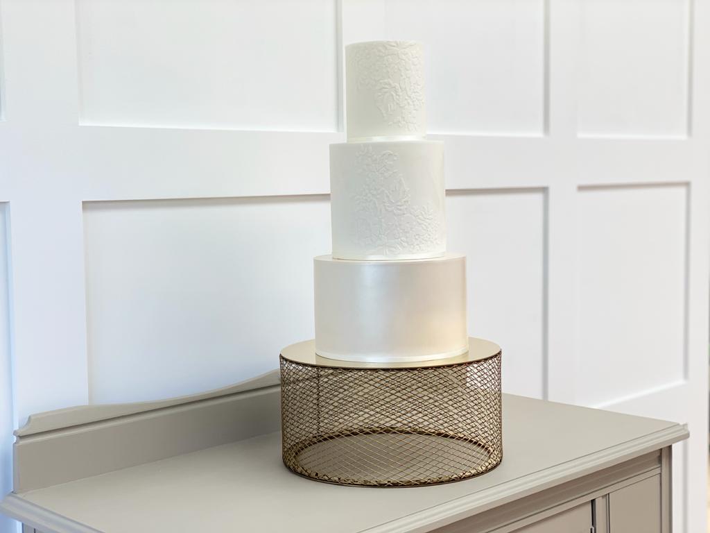 3 Tiered white detailed wedding cake on a 12" metallic gold mesh cake stand