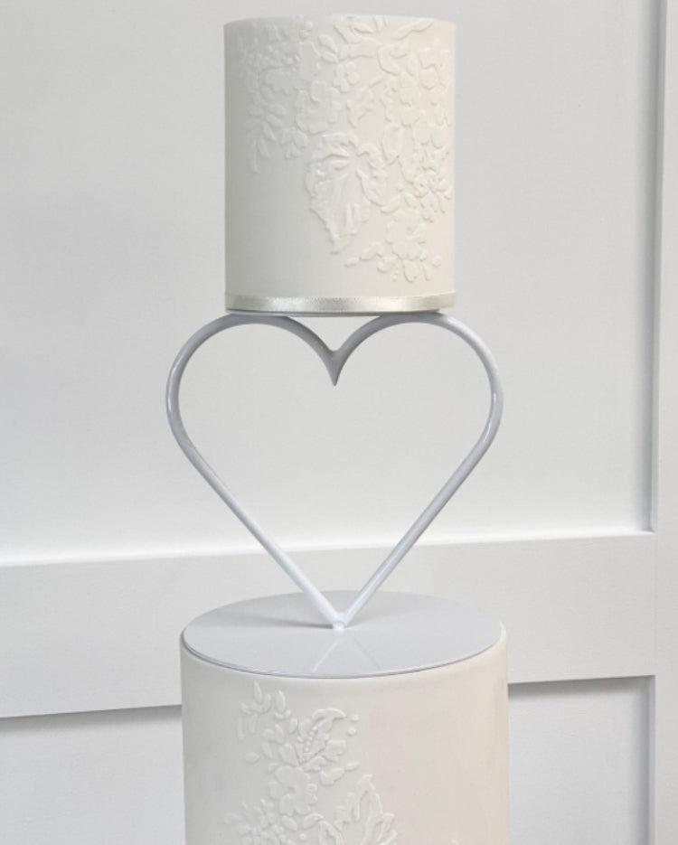 Two plain white cake layers with subtle floral patterns being separated by a Heart Tier Separator - Prop Options